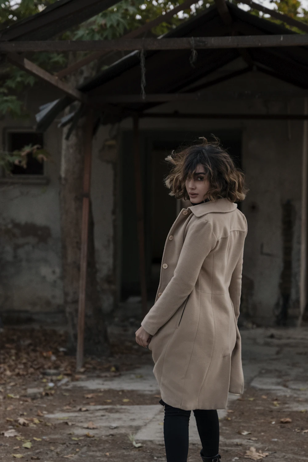 Une femme en trench devant un mur de pierre, de dos