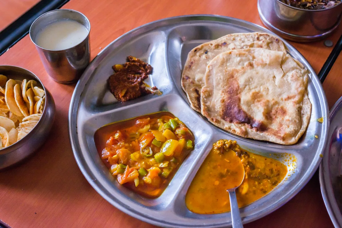 Un plateau en inox avec naans, curry de légumes et dal