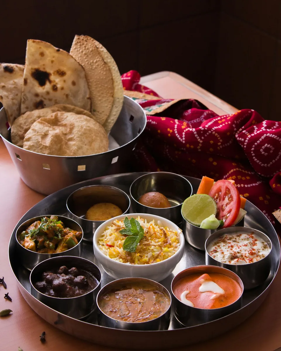 Un thali en coupelles, une corbeille de puris derrière