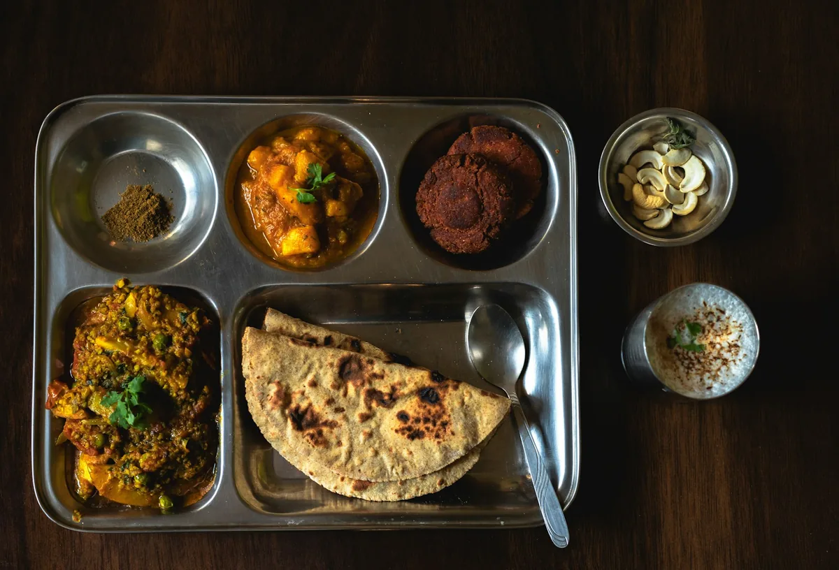 Un plateau en inox avec paratha, curry et épices